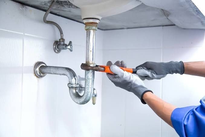 Minor plumbing works Singapore — plumber repairing under-sink pipe with wrench, HDB bathroom